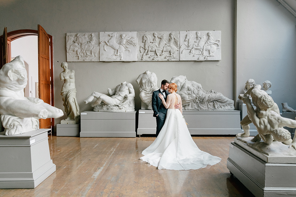 sweeping lace bridal gown with black suit for an art gallery wedding